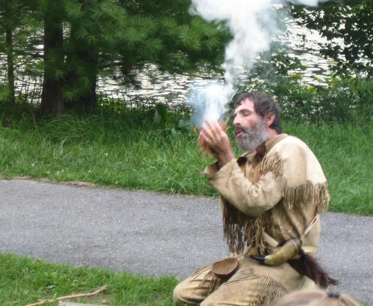 Man producing smoke with a bow drill fire set outdoors
