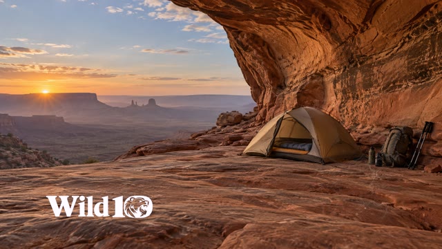 Modern backpacking gear beneath a sandstone alcove at desert dawn.