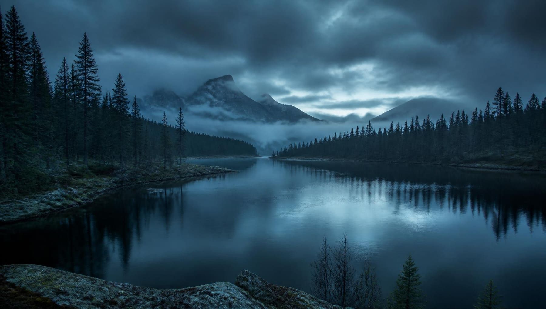 Dramatic snow-capped mountain ridge above a winding river valley at golden hour, with drifting clouds and rocky cliffs
